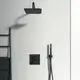 Ein schwarzer Duschkopf mit Handbrause und Thermostatsteuerung an einer weißen Wand. Handtuchhalter aus Metall. Ideal Standard Markenlogo sichtbar.